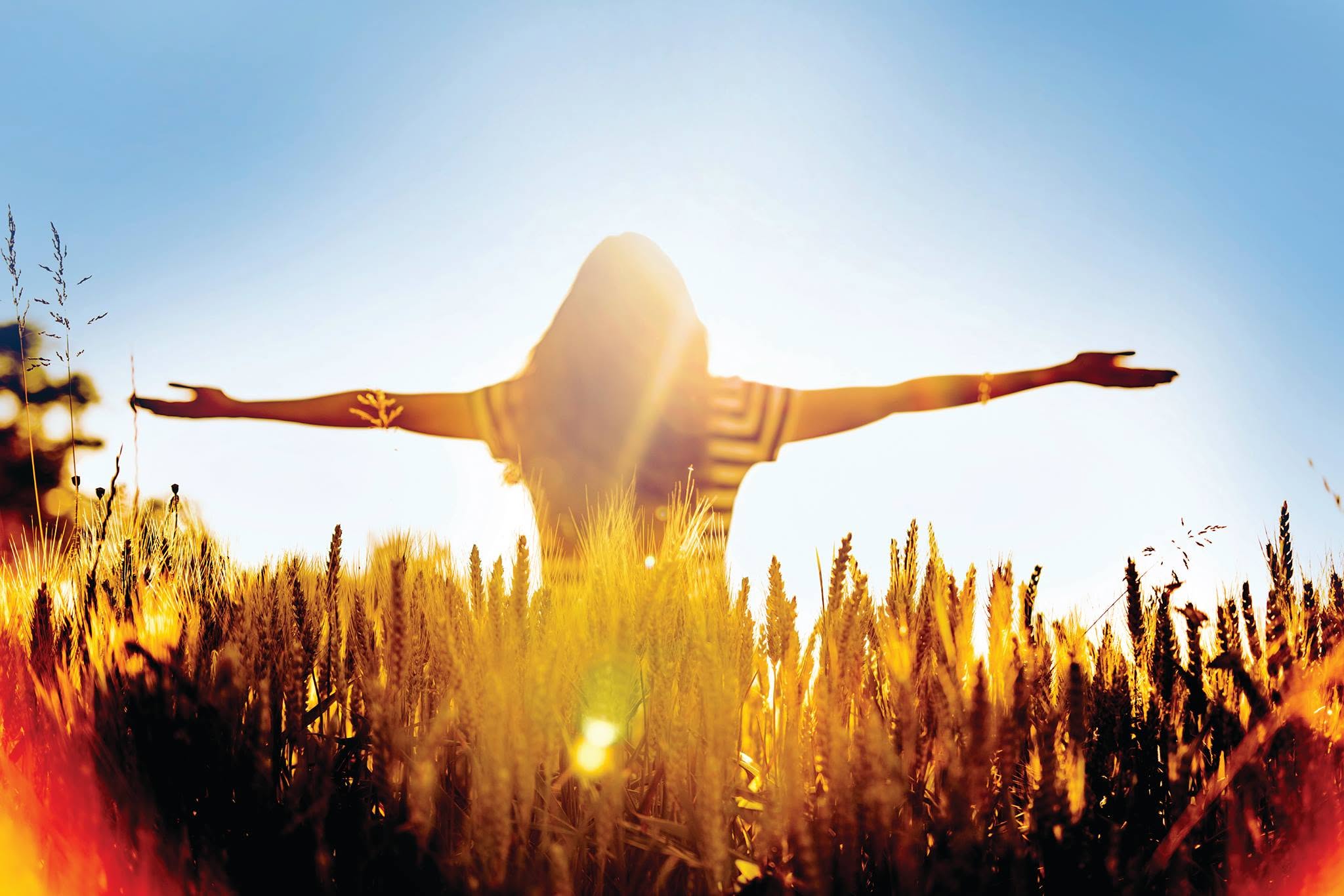 Une femme les bras ouverts dans un champ de blé baigné de soleil